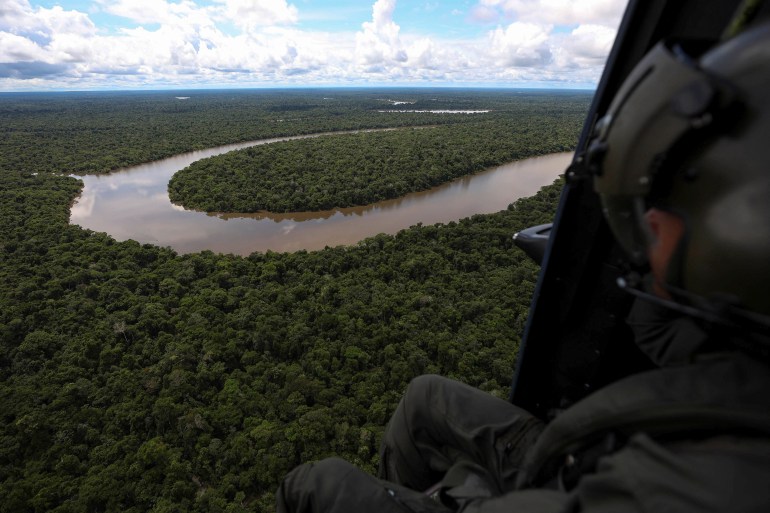Military rescue team fly anove a sweeping curve of the Itacoai River surrounded by dense forest