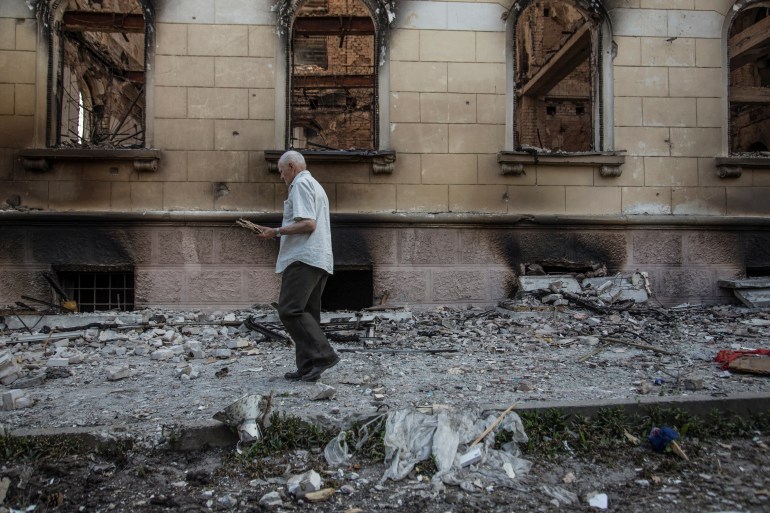 A man walks next to a building damaged by a military strike
