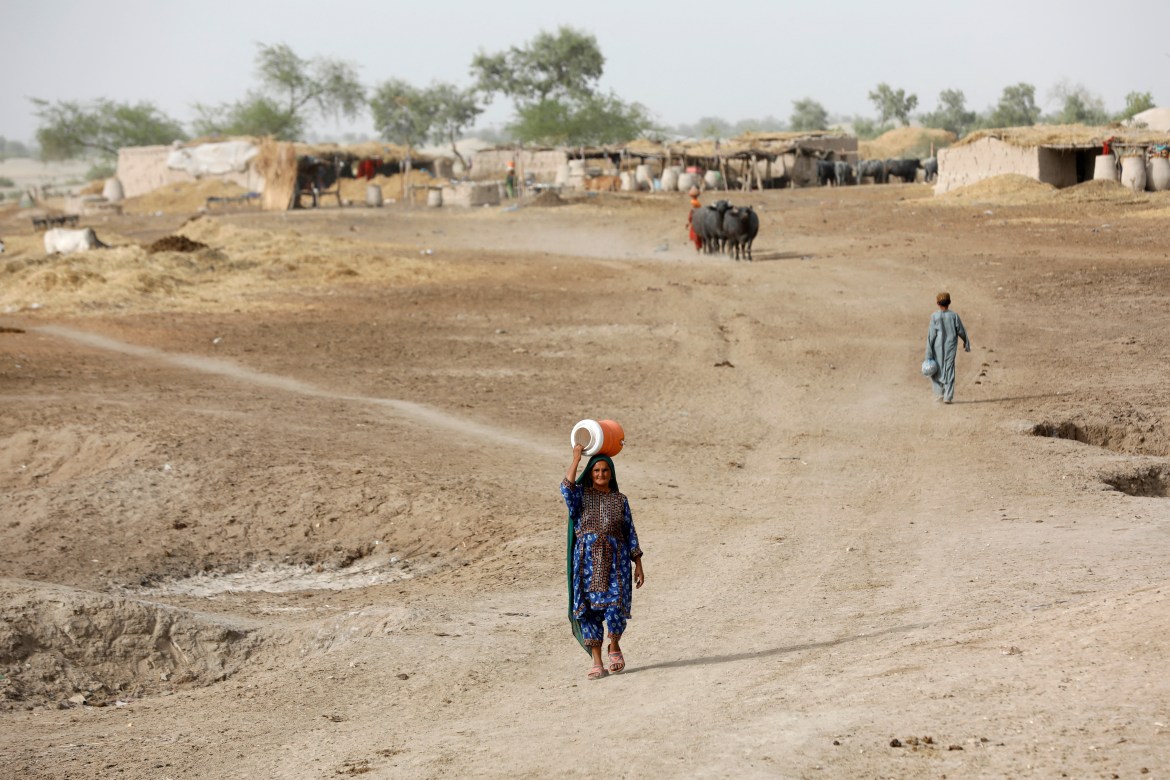 A woman walks to fetch water from a nearby hand-pump