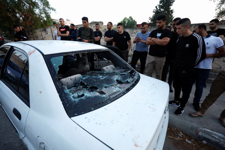 People look at a damaged vehicle following an Israeli raid in Jenin, in the Israeli-occupied West Bank.
