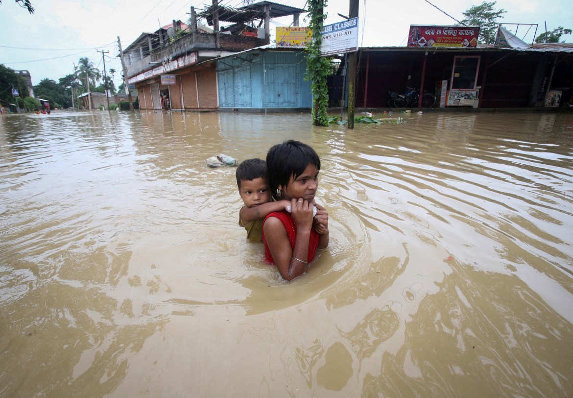A girl carries her brother as she wades through a flooded road after heavy rains, on the outskirts of Agartala, India,
