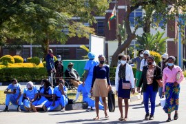 People walk past Zimbabwean medical workers as they sit outside Sally Mugabe Central Hospital during a strike by state doctors and nurses