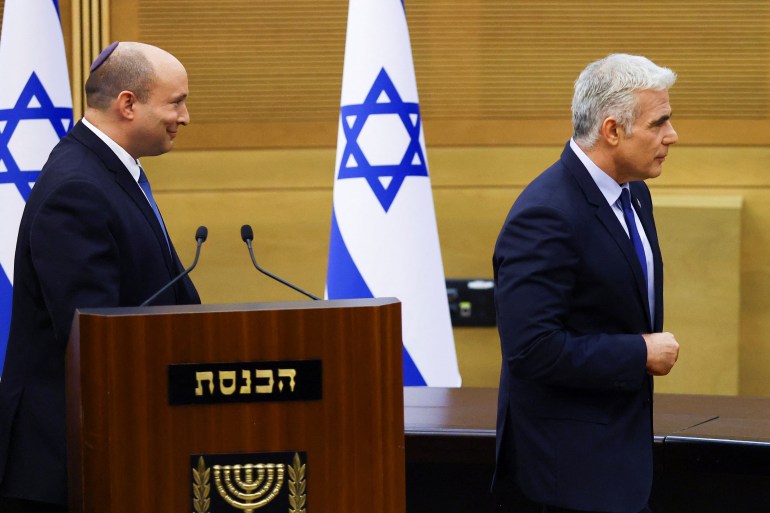 Naftali Bennett and Yair Lapid walk away from a podium with Israeli flags behind them