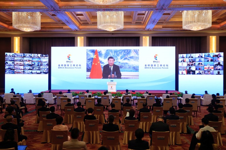 Xi Jinping speaks from a large screen to a virtual forum in Beijing with the audience sitting spaced apart on individual chairs because of COVID-19