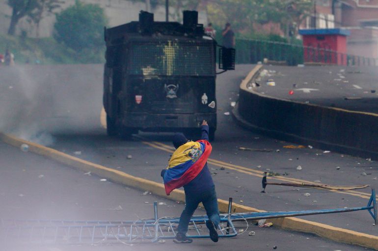 A demonstrator with an Ecuadorian flag throws a rock towards a police vehicle during an anti-government protest.