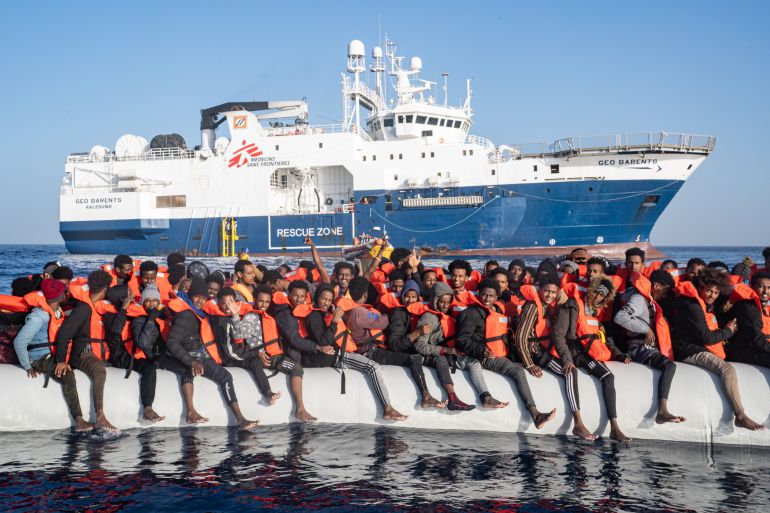People wearing life jackets wait to be transferred onto a ship in the Med Sea