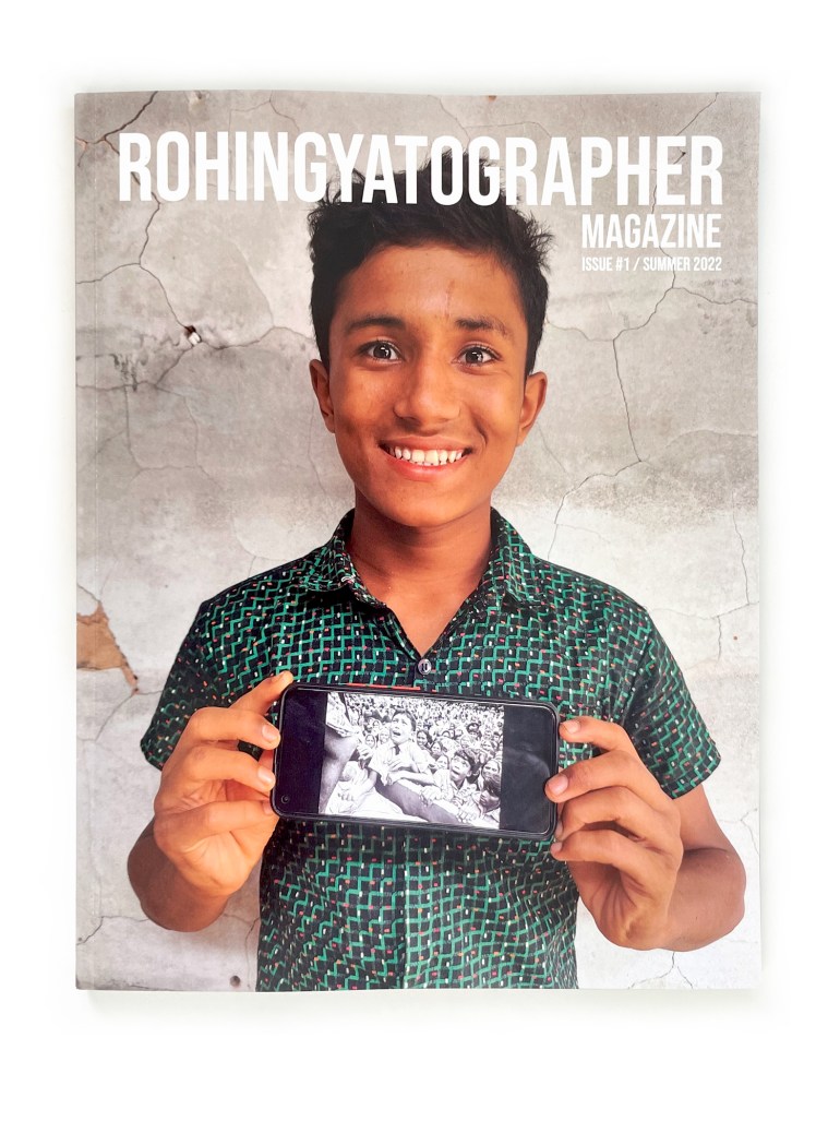 A young man in a green patterned shirt holds a photo on his mobile phone on the cover of Rohingya Tograh magazine