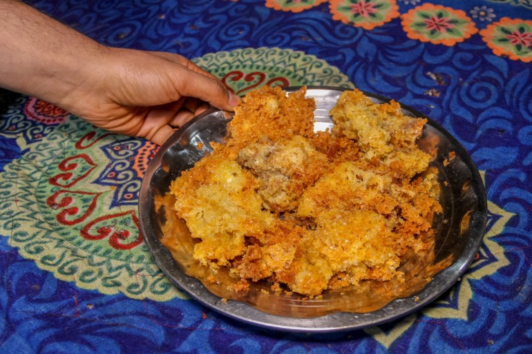 A hand holding a metal plate of fried kaladi, which has puffed up and gotten golden and crisp
