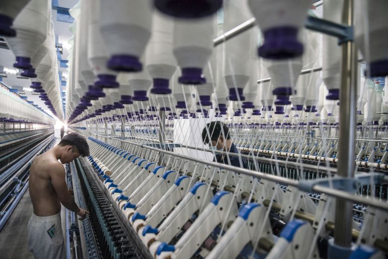 Workers stand in front of machines on a yarn production line at the Fujian Strait Textile Technology factory in Putian, Fujian province, China.