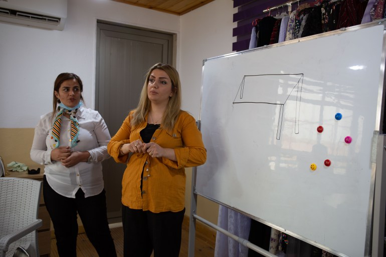 A photo of two women standing next to a whiteboard with a table drawn on it and some colourful magnets on the side of the board.