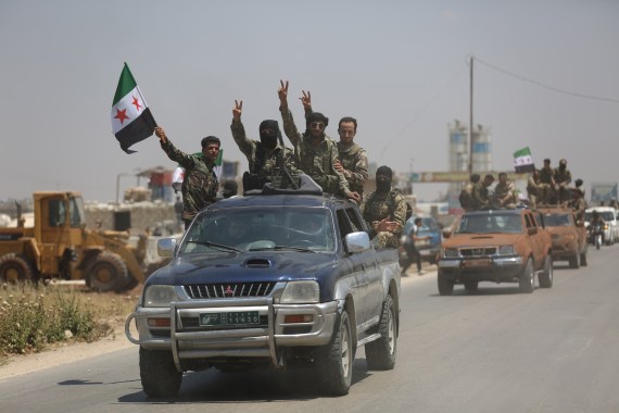 A group of fighters on top of a pick up truck wave the flag of the Syrian opposition