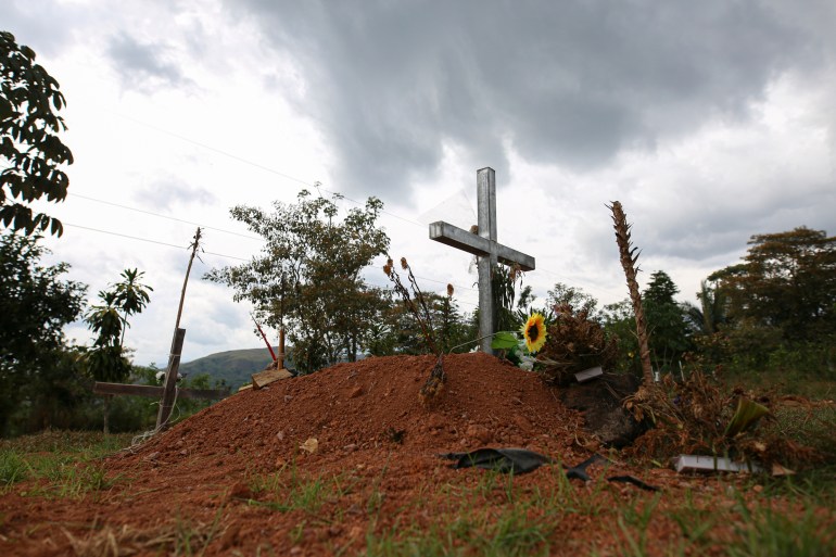 A photo of the grave of Sergio Rojas, with a cross on a little hill and a flower near the cross.