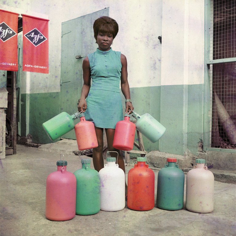 A photo of a woman holding four liquid containers with six other containers in a row in front of her.