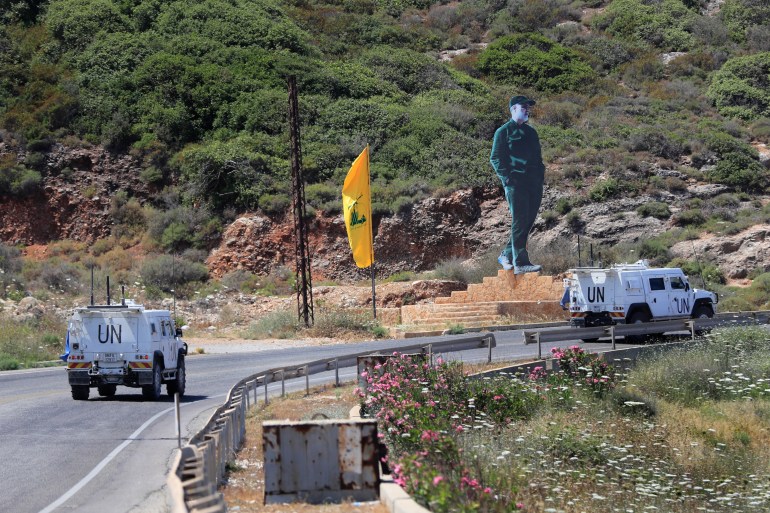 Vehicles of the United Nations peacekeeping force pass the Hezbollah flag and statue of the late Iranian general Qassem Soleimani, as they patrol a road along the Lebanon-Israel border town of Naqoura, Lebanon