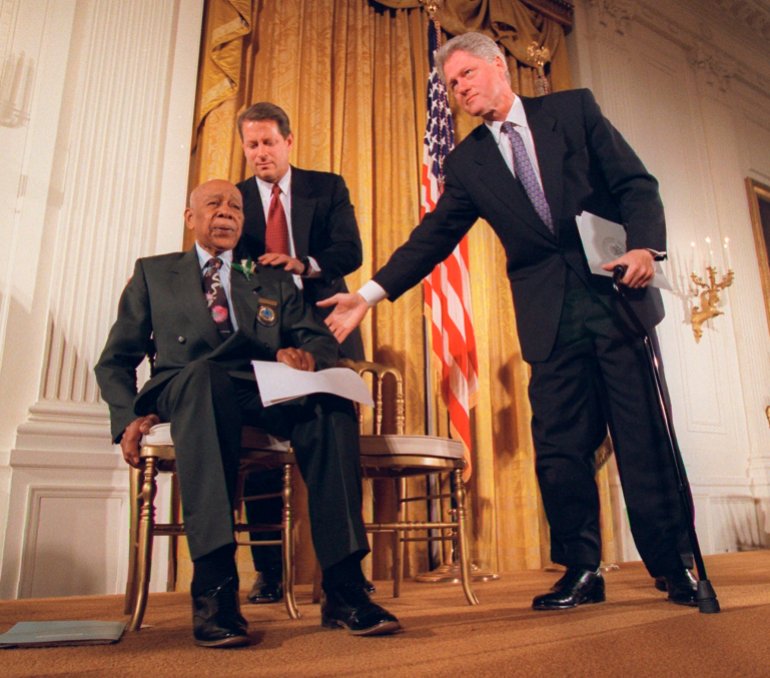US President Bill Clinton and Vice President Al Gore, back, help Herman Shaw, 94, a Tuskegee Syphilis Study victim, during a news conference in 1997 [File photo: Doug Mills/AP]