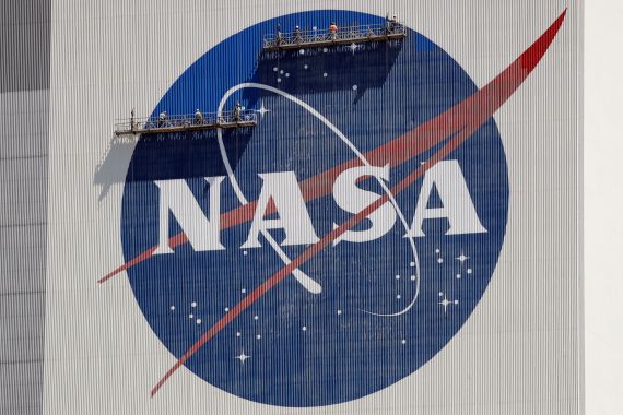Workers on scaffolding repaint the NASA logo on the side of a building