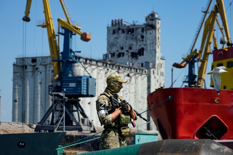 A Russian soldier guards a pier with grain storage facilities the background at Ukraine's Mariupol Sea Port on June 12, 2022 [File: AP]