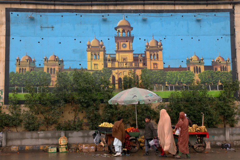 A family walk past a huge mural of historical Islamia College building painted on an overhead bridge wall, in Peshawar, Pakistan, Friday, Jan. 7, 2022.