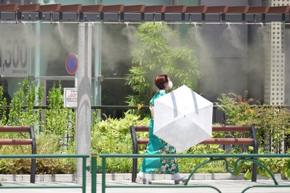 A person wearing face masks to help protect against the spread of the coronavirus walks by a cooling mist spot Tuesday, June 28, 2022 in Tokyo
