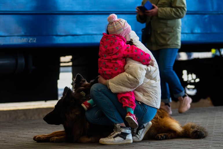 A woman holds a child and dogs on a train platform after arriving from Mariupol