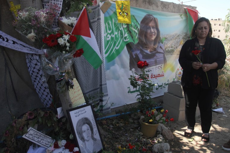 A Palestinian woman arranges flowers at the site where Al-Jazeera reporter Shireen Abu Akleh was killed in the occupied West Bank city of Jenin.