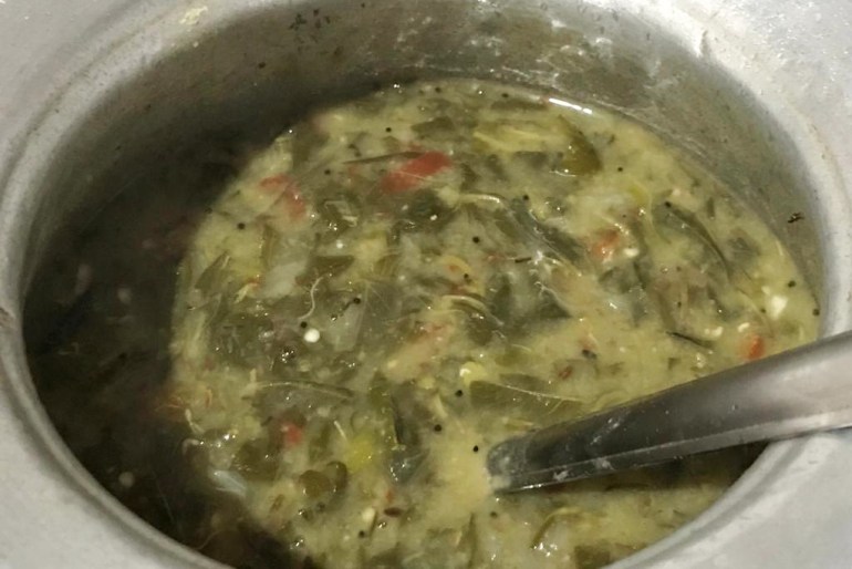 A pot of mixed greens curry with a stainless sleel ladle in it
