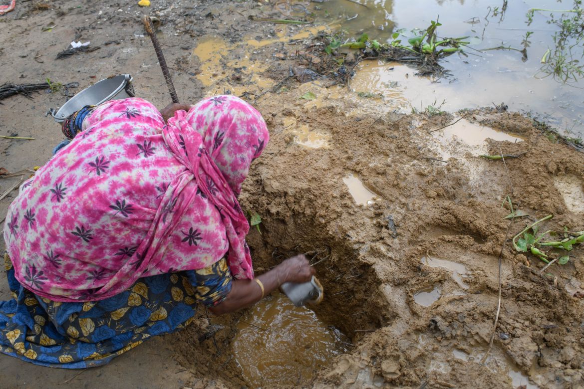 An woman taking shelter in the relief camp digs a hole in the ground to find water in Kholahat Reserve Forest,