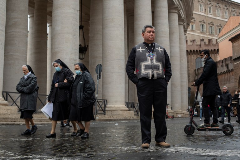 A photo of Reverend Maurice Henry Sands standing in St Peters Square in Rome Italy with a group of three nuns walking behind him on one side and a person on a scooter on the other side.