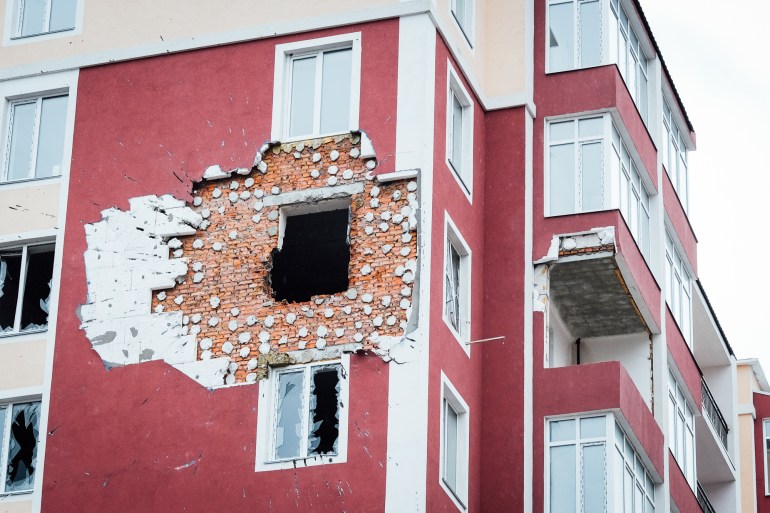 A photo of a building with shattered windows and a large hole in the wall.