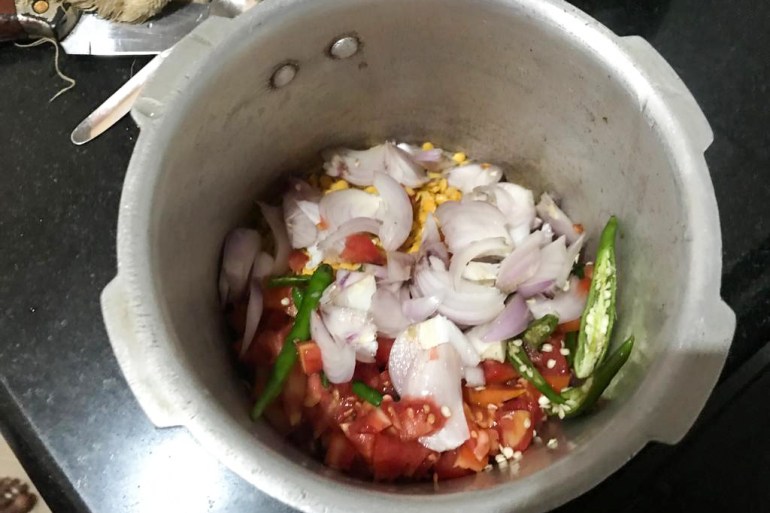 A photo of a pressure cooker with all the ingredients for a wild greens curry in it