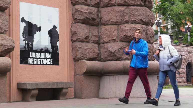 Jóvenes ucranianos en el centro de Kyiv junto a un cartel de guerra