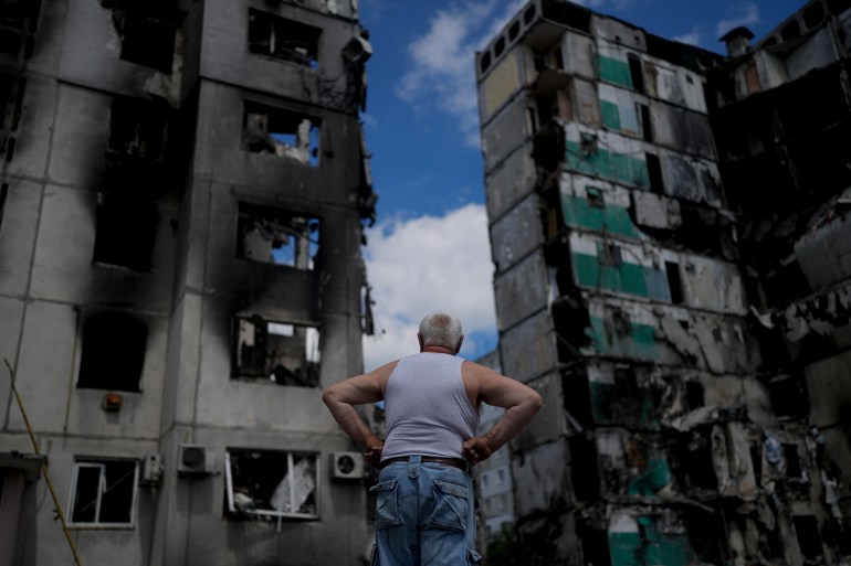 A man is seen looking at a destroyed building on the outskirts of Kyiv
