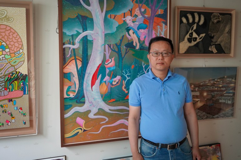 Lim Sang-jin posing in front of a wall filled with paintings.