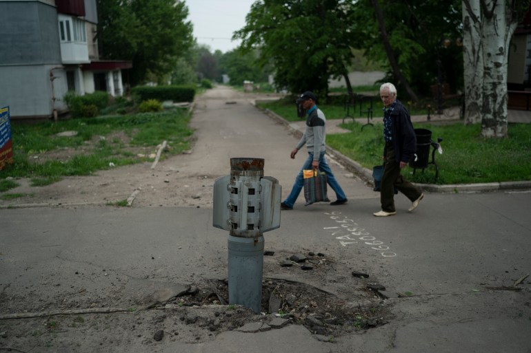 People walk past part of a rocket that sits wedged in the ground in Lysychansk, Luhansk region, Ukraine, Friday, May 13, 2022