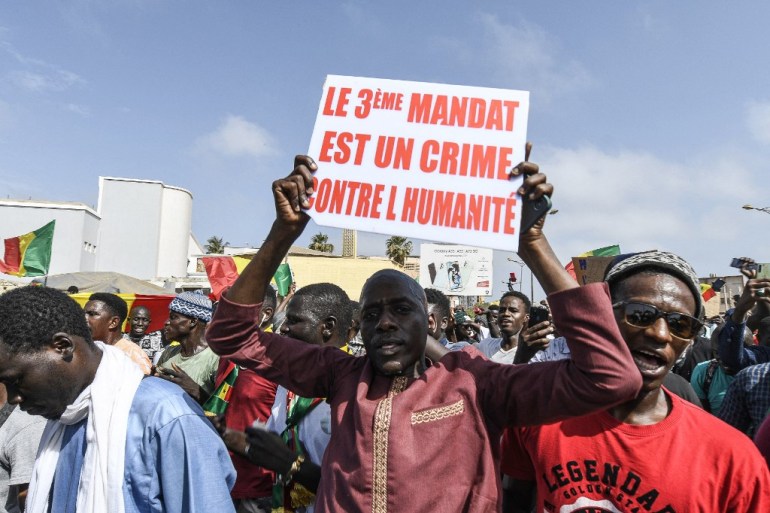A protestor holds a sign reading "The 3rd mandate is a crime against humanity" as he attends a rally of the Senegalese opposition at the Place de l'Obelisque in Dakar