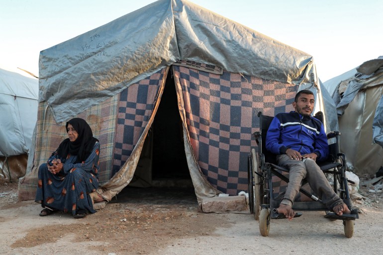 A disabled man sits in a wheelchair near a woman outside a tent at the "Blue camp" for Syrians displaced by conflict near the town of Maaret Misrin in the rebel-held northern part of the northwestern Idlib province during the Muslim holiday of Eid al-Adha on July 10, 2022. 
