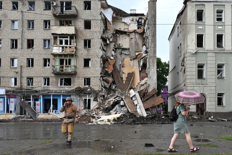 A local resident walks past a Ukrainian rescuer working outside a building partially destroyed after a Russian missile strike in Kharkiv on July 11, 2022, amid Russia's military invasion launched on Ukraine.