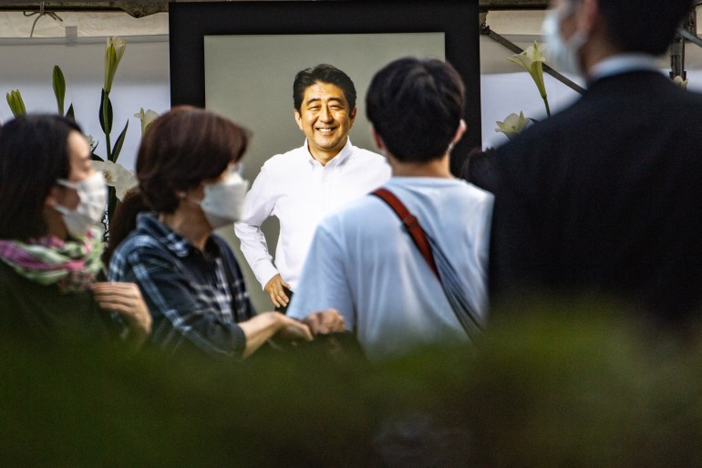 People offer flowers in front of a portrait of a smiling and relaxed Shinzo Abe, who was assassinated on Friday