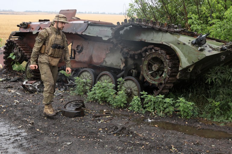 Ukrainian serviceman walks past a destroyed armoured personnel carrier near the front line in the south of Kharkiv region