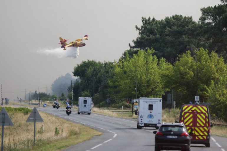 A Canadair plane drops water along the departmental road 112 while a fire is currently heading towards the town of Cazaux 