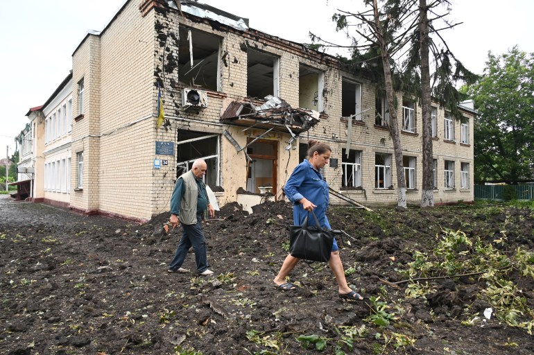 Local residents walk past a damaged building partially destroyed after a shelling in the city of Chuguiv, east of Kharkiv, on July 16, 2022. - In the northeast region around Ukraine's second city of Kharkiv, governor Oleg Synegubov said an overnight Russian missile attack killed three people in the town of Chuguiv.
