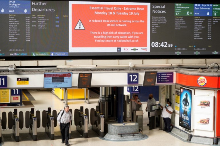 Commuters walk under a message board warning people of disruption over extreme heat at Victoria Station in London 