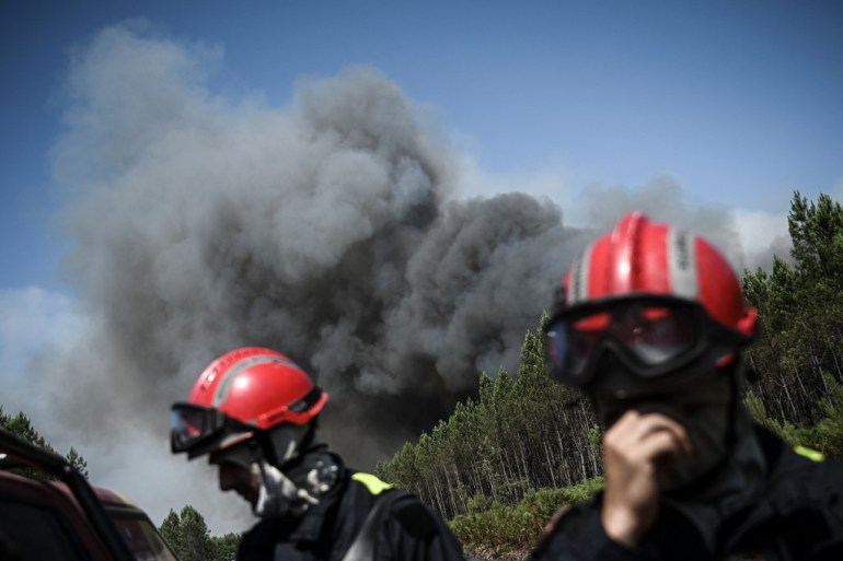 Firefighters stand on a road as heavy smoke is seen in the background during forest fires near the city of Origne, south-western France