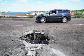 A car moving past a crater on Kherson&#39;s Antonivskiy bridge across the Dnieper River caused by a Ukrainian rocket attack [AFP]