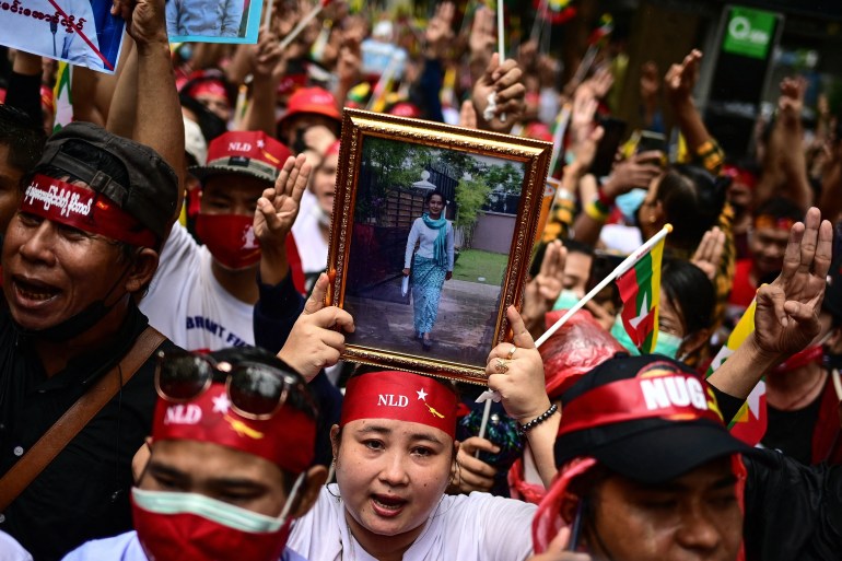 معترضان با سه انگشت سلام می دهند و عکس های آنگ سان سوچی رهبر غیر نظامی زندانی میانمار را در دست دارند.