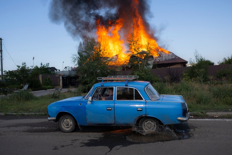 A Ukrainian man drives past a burning house hit by a shell in the outskirts of Bakhmut, Eastern Ukraine, on July 27, 2022