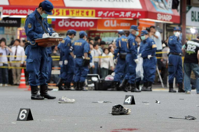 Police on a blood-stained street in Akhibara investigate the aftermath of Kato's stabbing attack watched by a crowd of onlookers in Tokyo, Japan.