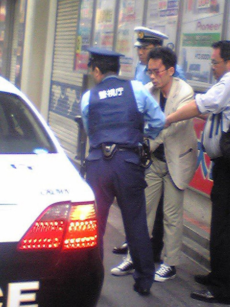 Police arrest Tomohiro Kato, who is wearing a beige suit and glasses, on a street in Akhibara after he killed seven people in Tokyo.