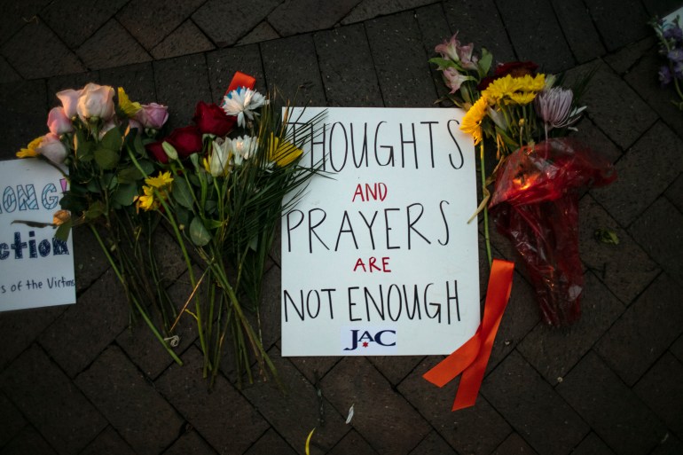 A sign that reads 'Thoughts and prayers are not enough' on the ground with flowers around it at a vigil in Highland Park, Illinois.
