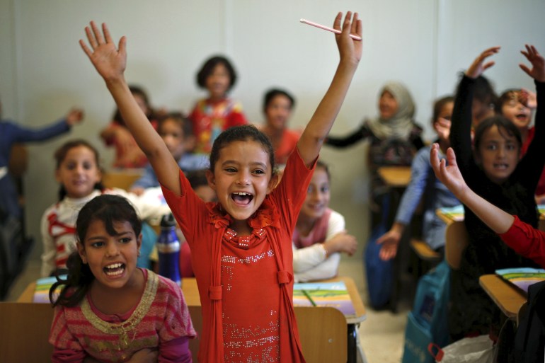 طلاب لاجئون سوريون يشيرون أثناء حضورهم فصلًا في إحدى مدارس اليونيسف